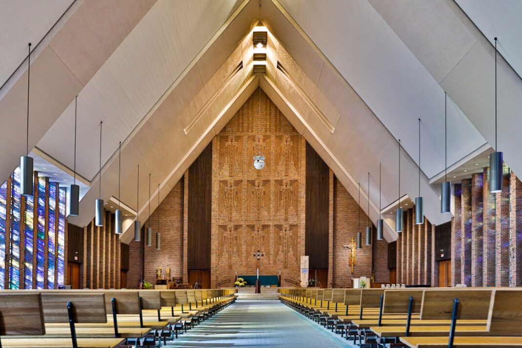 The interior of an A-frame church with rows of seating on either side of the aisle and modern lighting overhead.